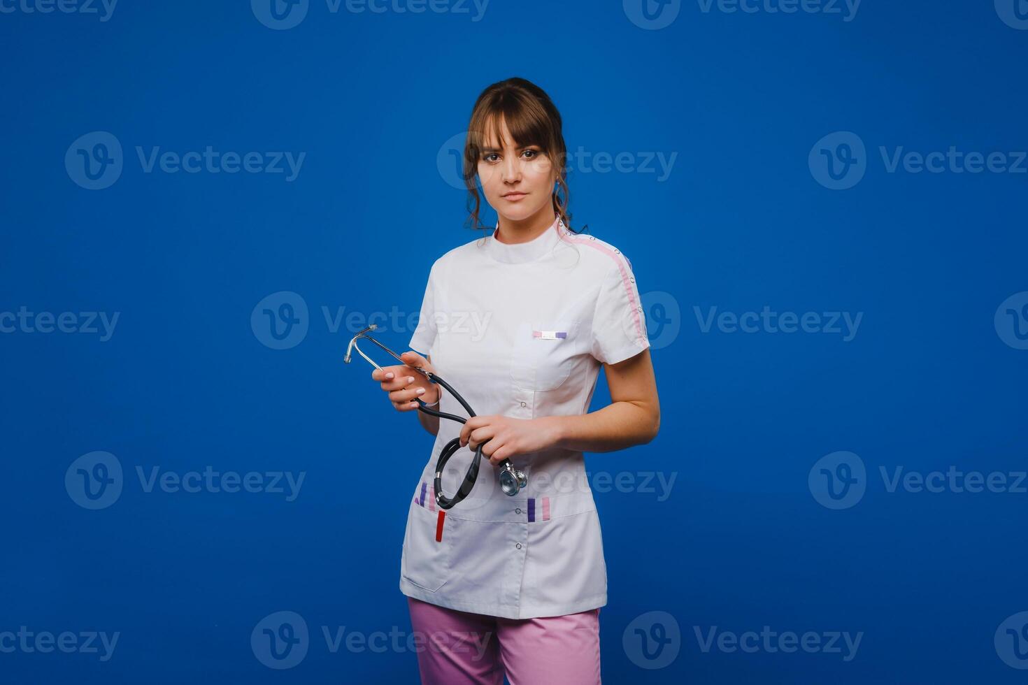 A female doctor, gesticulating, checks the heartbeat in the doctor's office at the hospital with a stethoscope isolated on a blue background photo