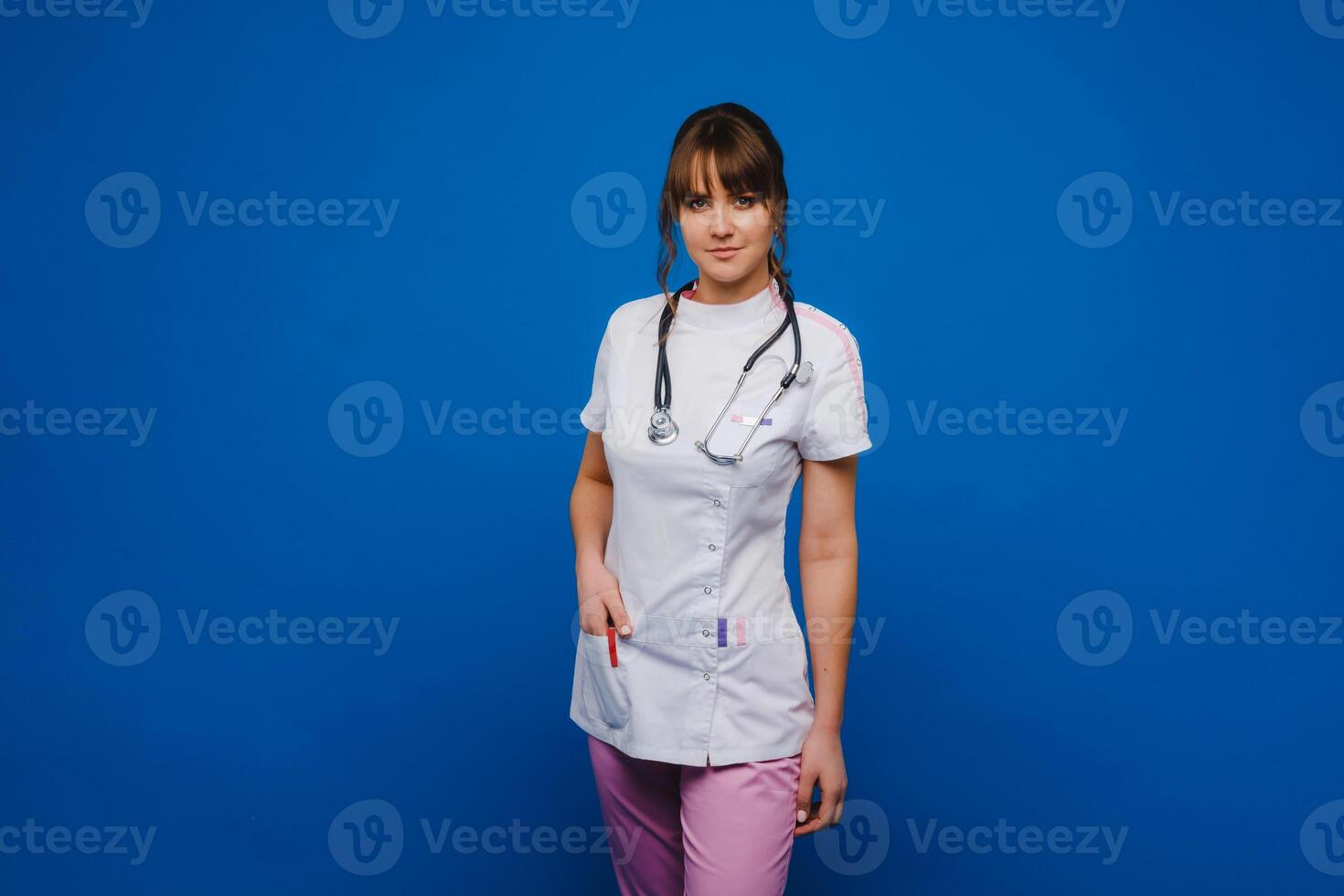 A female doctor, gesticulating, checks the heartbeat in the doctor's office at the hospital with a stethoscope isolated on a blue background photo