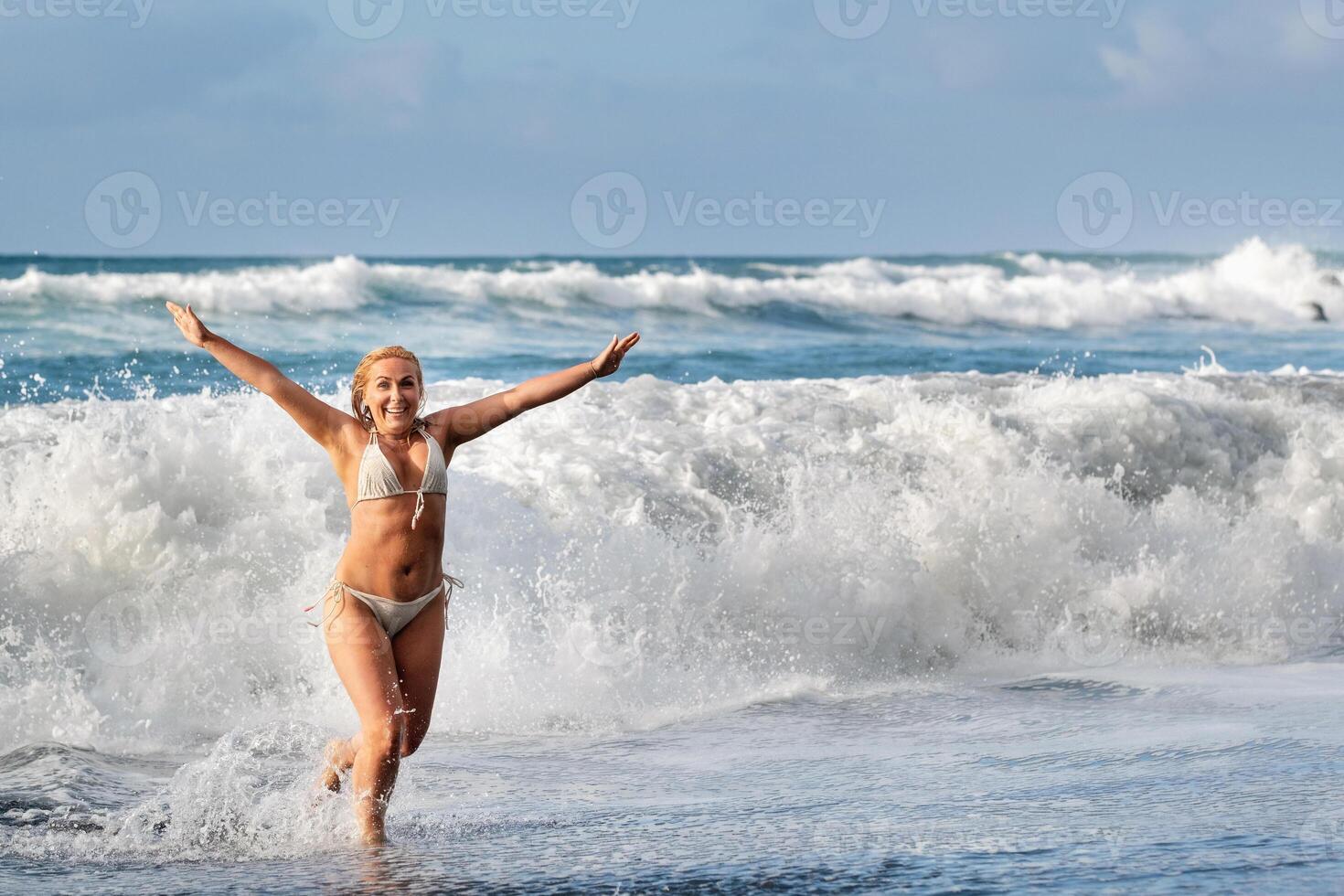 un niña con mojado pelo saltos terminado grande olas en el atlántico océano, alrededor un ola con salpicaduras de rociar y agua gotas.tenerife.españa foto