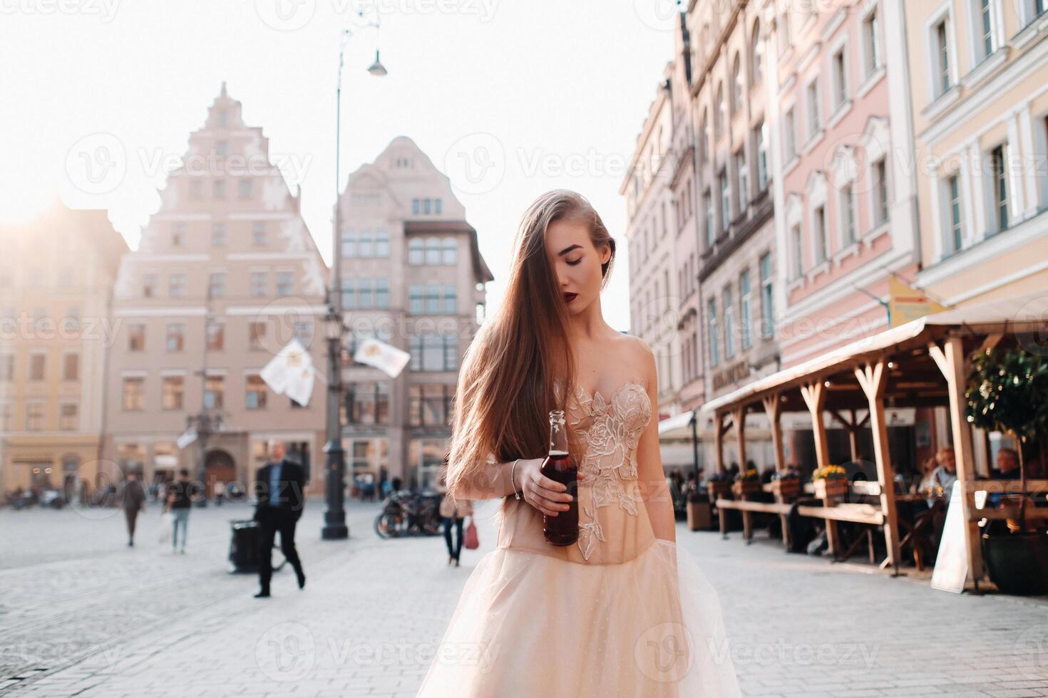 A bride in a wedding dress with long hair and a drink bottle in the Old town of Wroclaw. Wedding photo shoot in the center of an old Polish city.Wroclaw, Poland