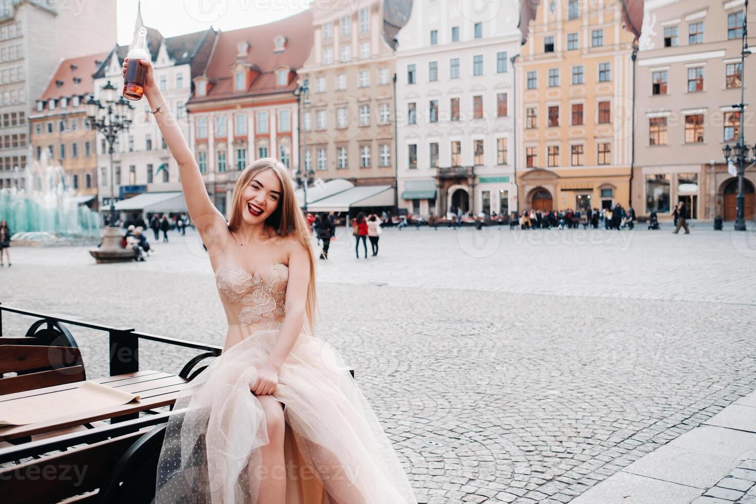 A bride in a wedding dress with long hair and a drink bottle in the Old town of Wroclaw. Wedding photo shoot in the center of an old Polish city.Wroclaw, Poland