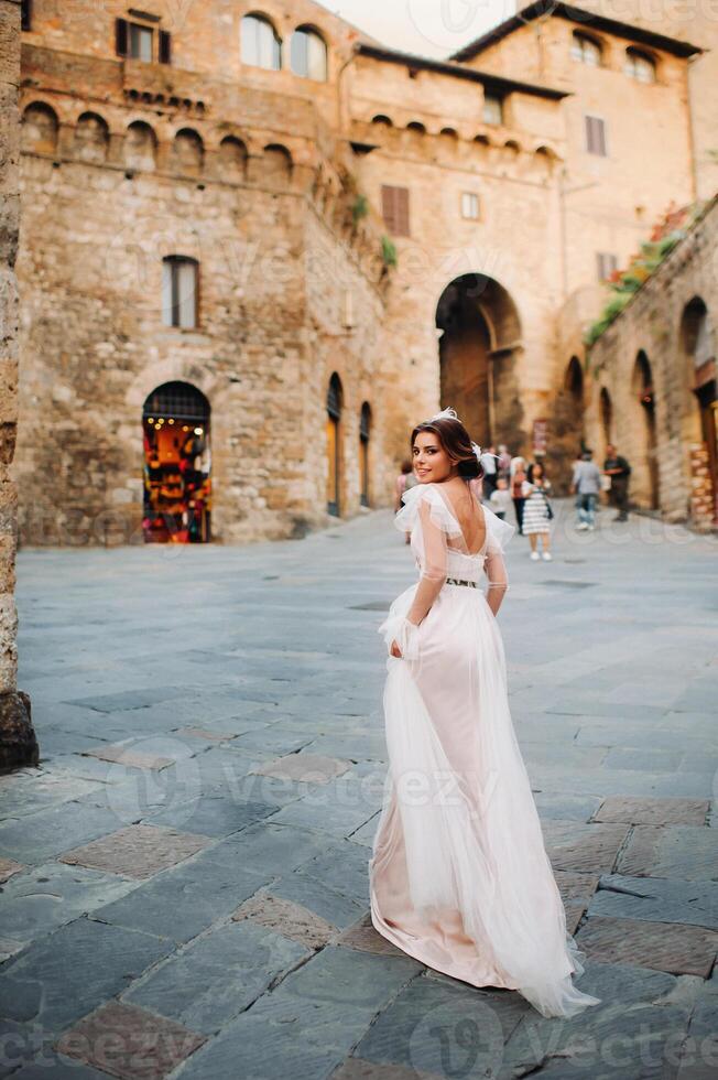 A bride in a white dress in the old town of San Gimignano.A girl walks around the city in Italy.Tuscany. photo