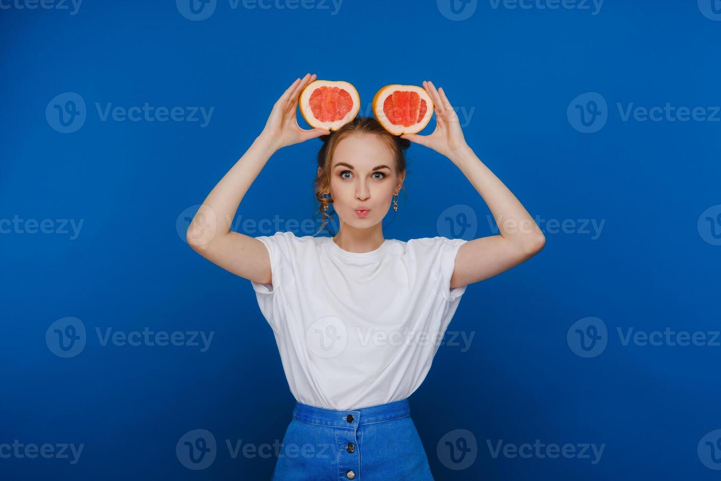 Surprised, the laughing girl holds the grapefruit like ears. Vegan lifestyle. Smiling woman , eating concept.Diet organic , weight loss and healthy food. Smoothies and fresh juice. photo