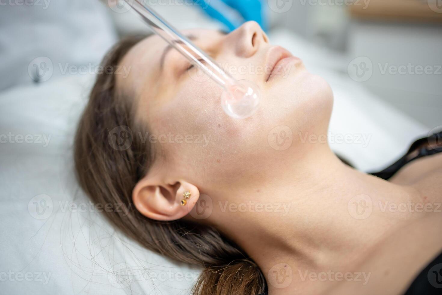Beautician uses the darsonval device on the client's face. Professional skin care in the salon. The concept of cosmetology and rejuvenation. photo