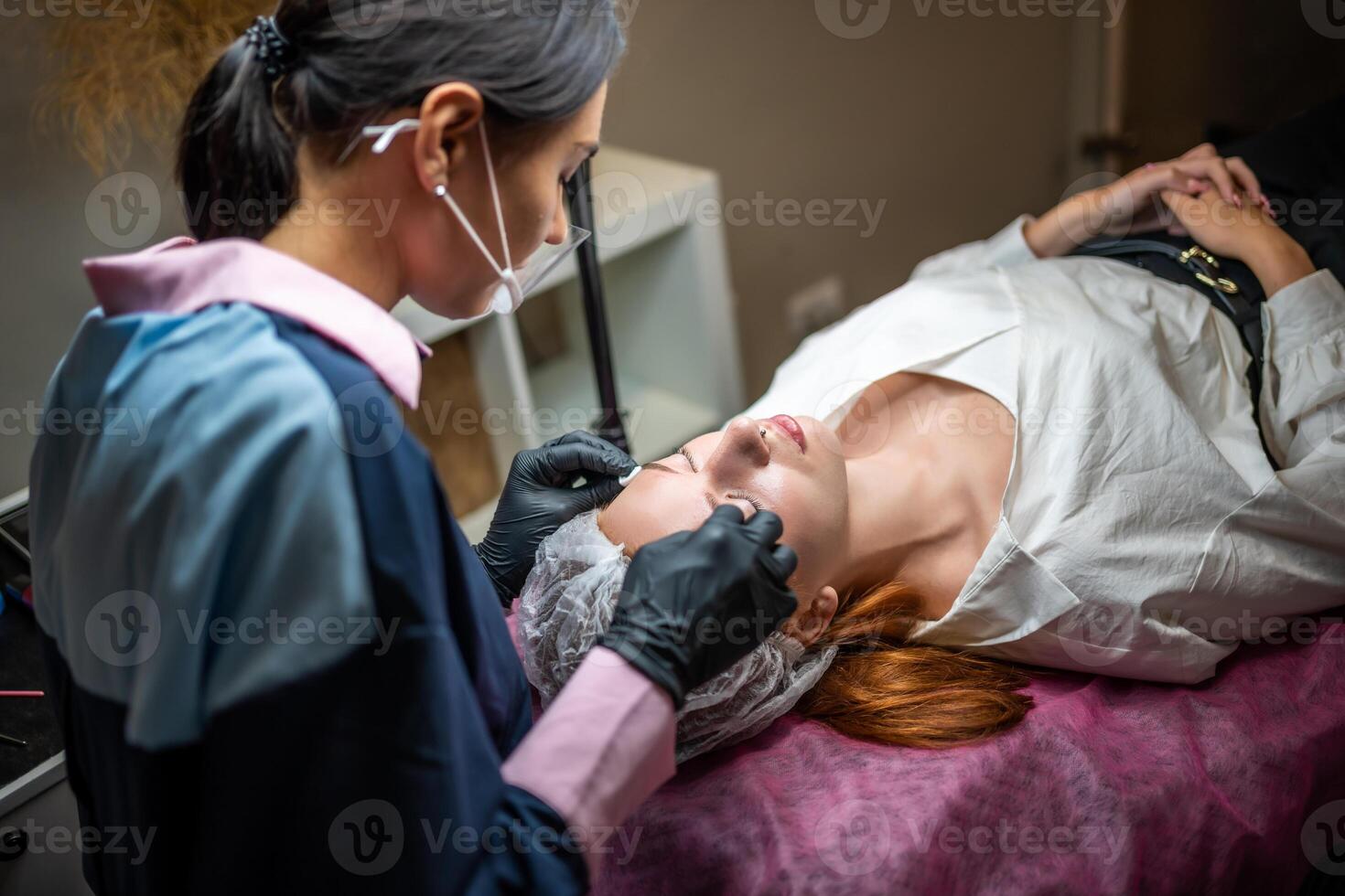 Procedure of eyebrow microblading. A master in black gloves is doing a blending needle of model's brow. photo
