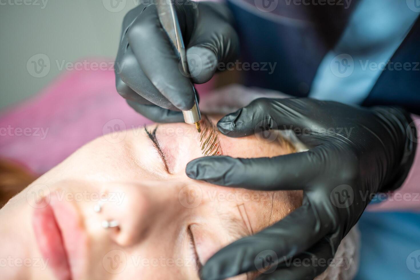 Procedure of eyebrow microblading. A master in black gloves is doing a blending needle of model's brow. photo