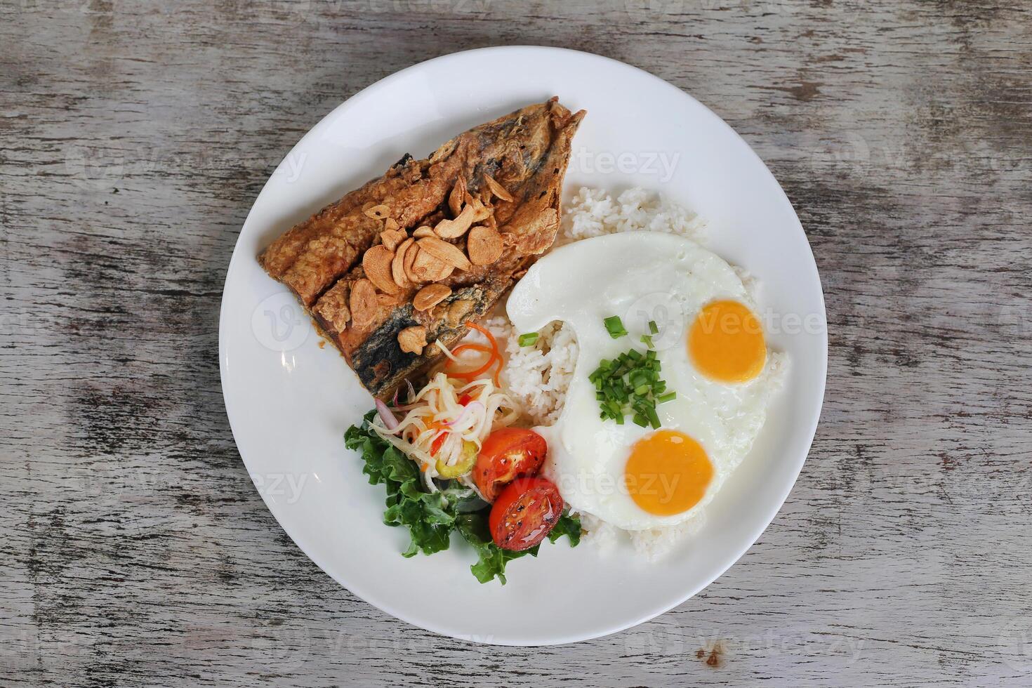 Daing Na Bangus with sunny egg and rice with tomato with salad served in dish isolated on wooden background top view of breakfast photo