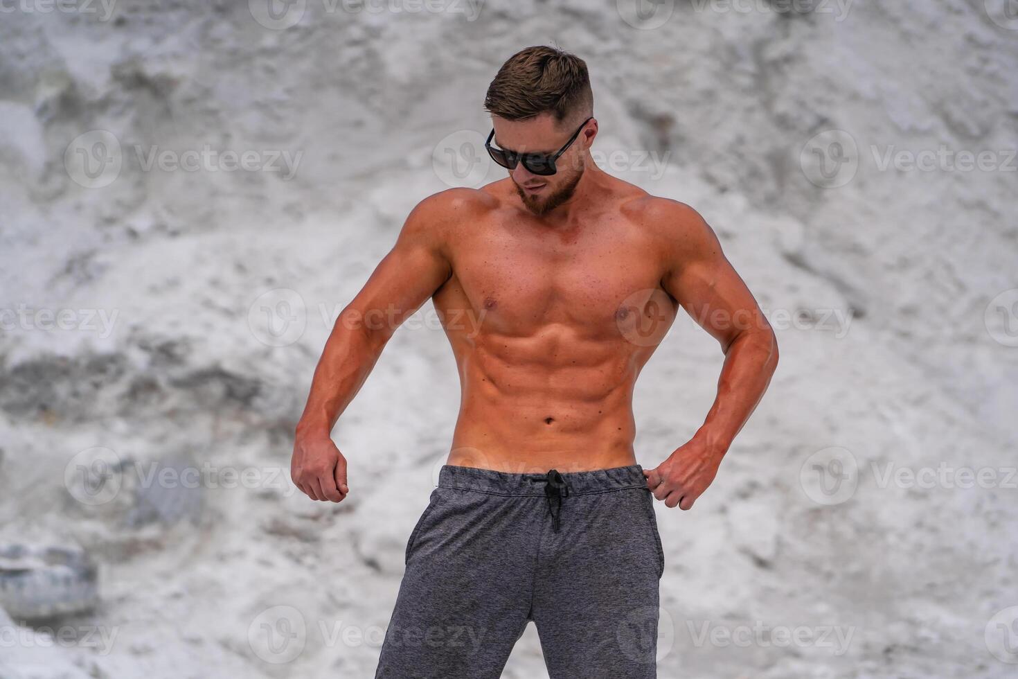 in sunglasses posingoutdoor. Preparing for training in a quarry. Photoshoot in white mountains. Strong attractive bodybuilder. Lifestyle. White landscape. photo