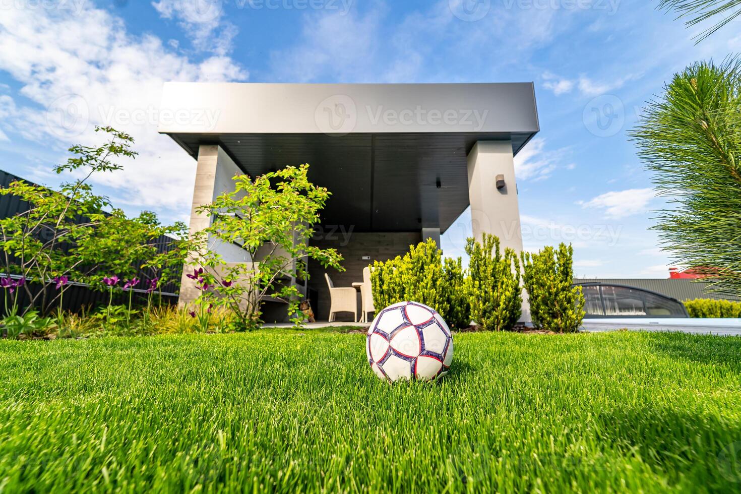 Ball on green lawn. Modern out-to-date house background. Blue sky above. Nobody in the yard. Football ball on the lawn. Modern architecture. photo