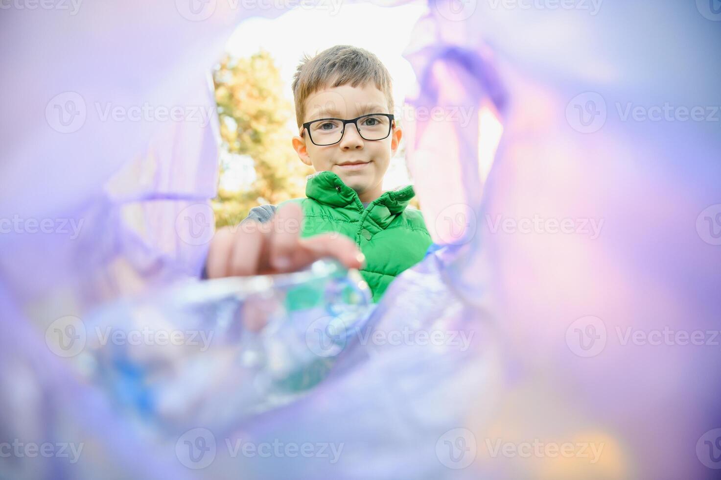 Environmental conservation concept.Little boy collects garbage and plastic bottles in the street to throw them in the trash bin photo