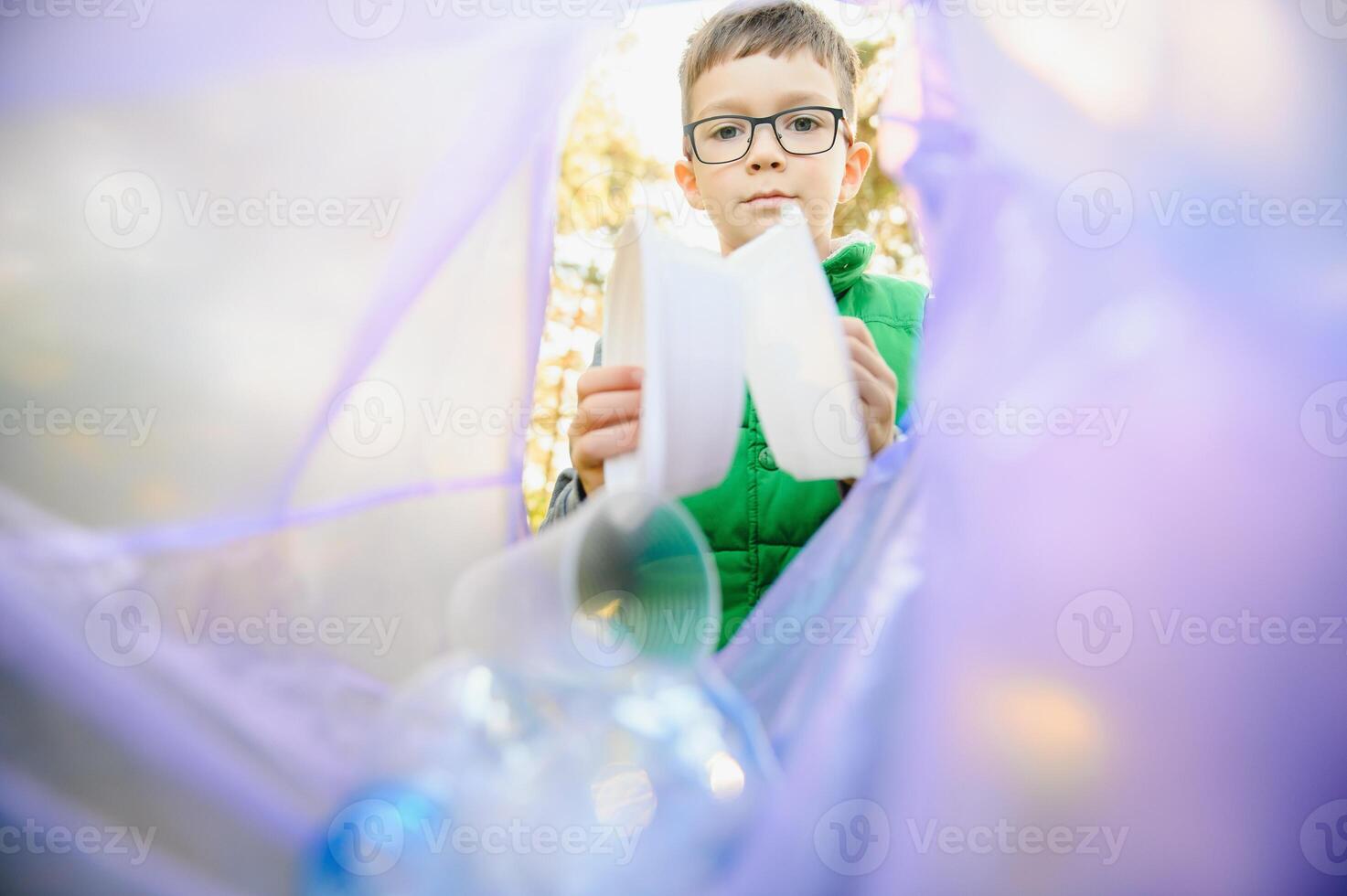 Environmental conservation concept.Little boy collects garbage and plastic bottles in the street to throw them in the trash bin photo