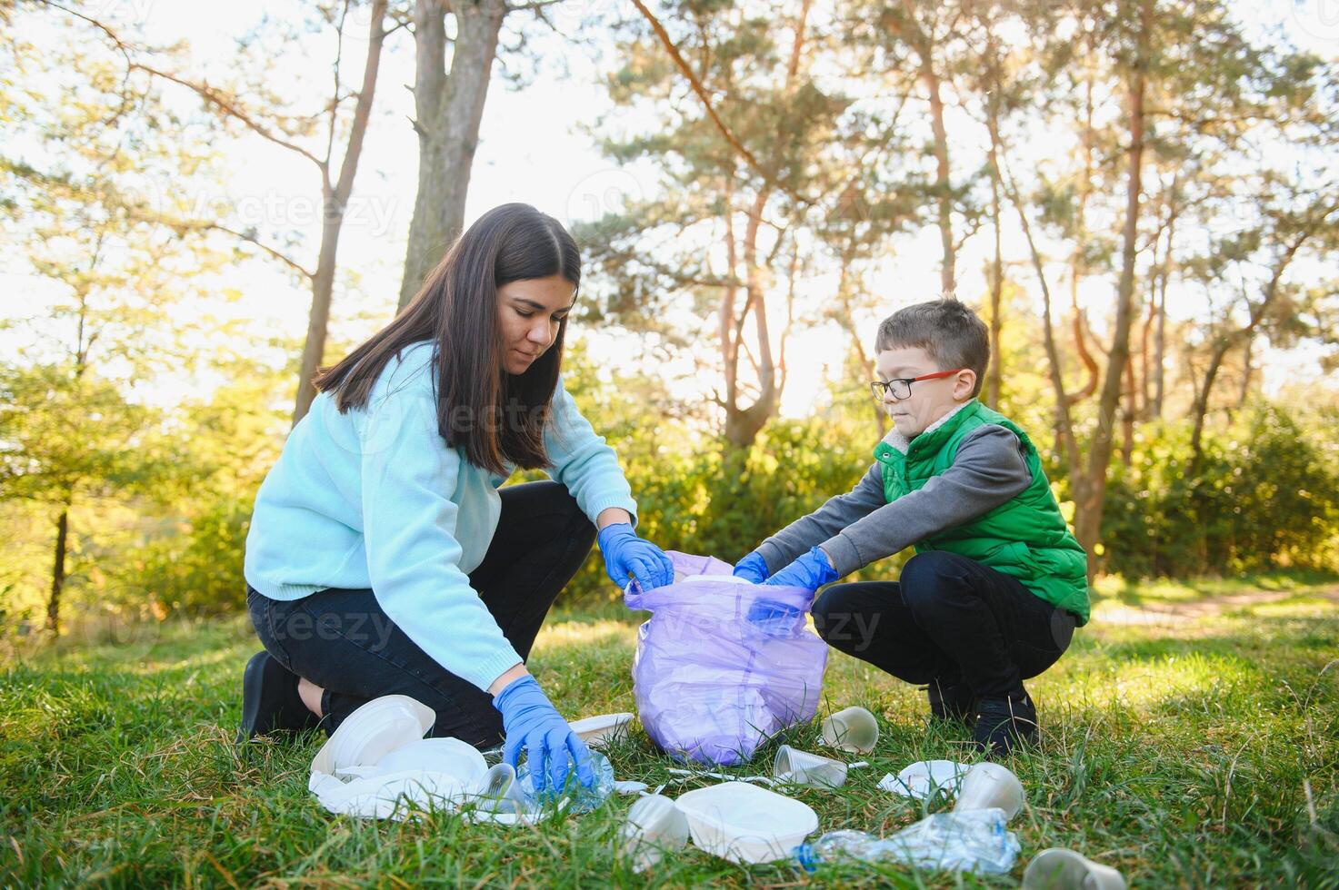 Woman volunteer and little boy picking up the plastic garbage and putting it in biodegradable trash-bag outdoors. Ecology, recycling and protection of nature concept. Environmental protection. photo
