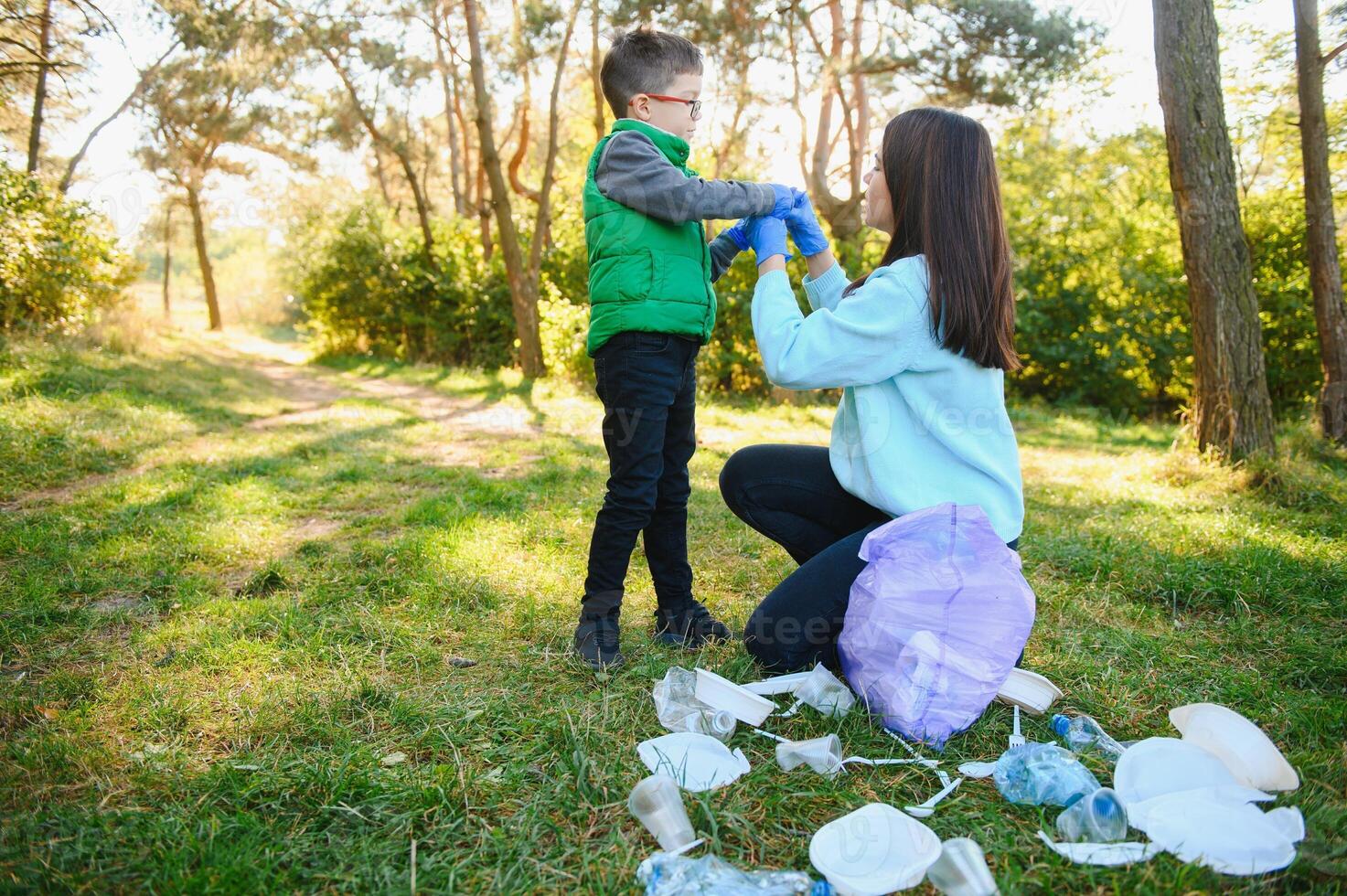 Woman volunteer and little boy picking up the plastic garbage and putting it in biodegradable trash-bag outdoors. Ecology, recycling and protection of nature concept. Environmental protection. photo
