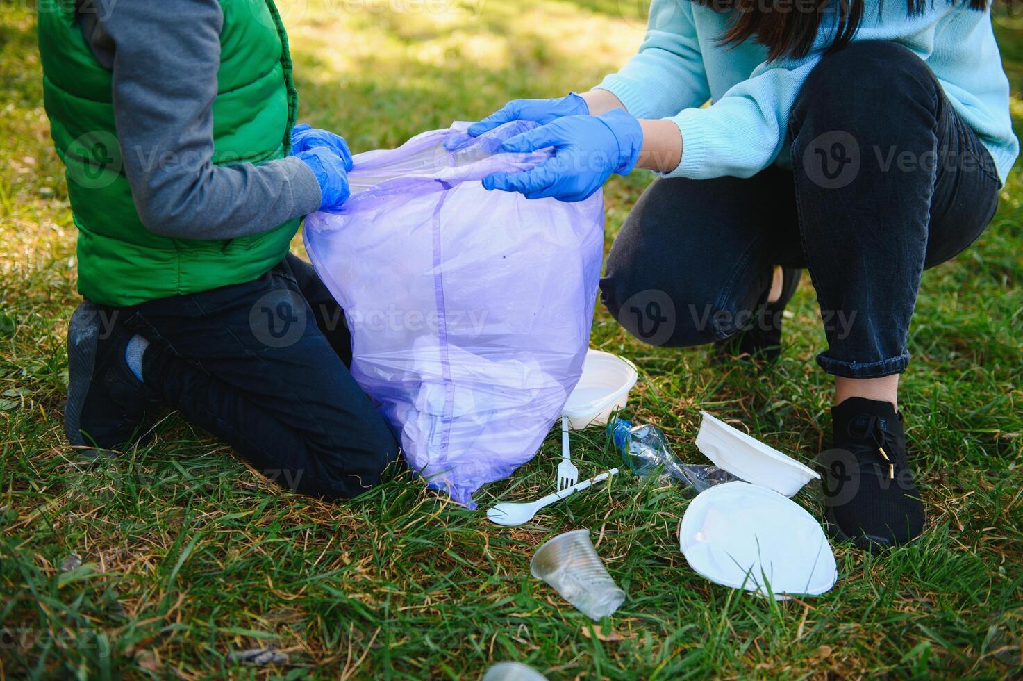 Woman volunteer and little boy picking up the plastic garbage and putting it in biodegradable trash-bag outdoors. Ecology, recycling and protection of nature concept. Environmental protection. photo