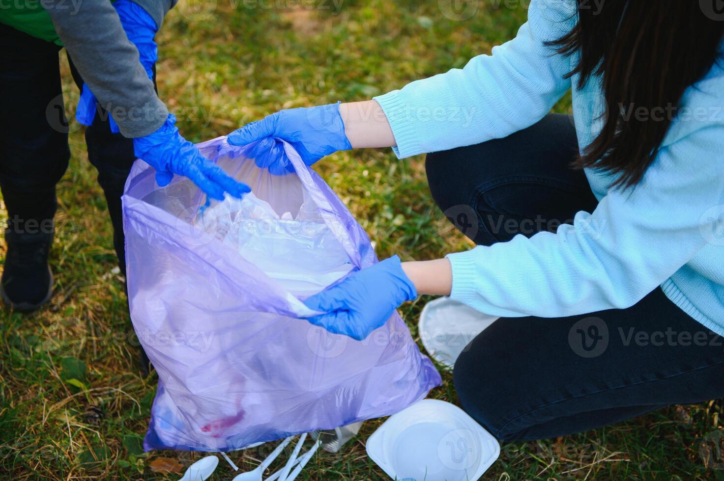 Woman volunteer and little boy picking up the plastic garbage and putting it in biodegradable trash-bag outdoors. Ecology, recycling and protection of nature concept. Environmental protection. photo