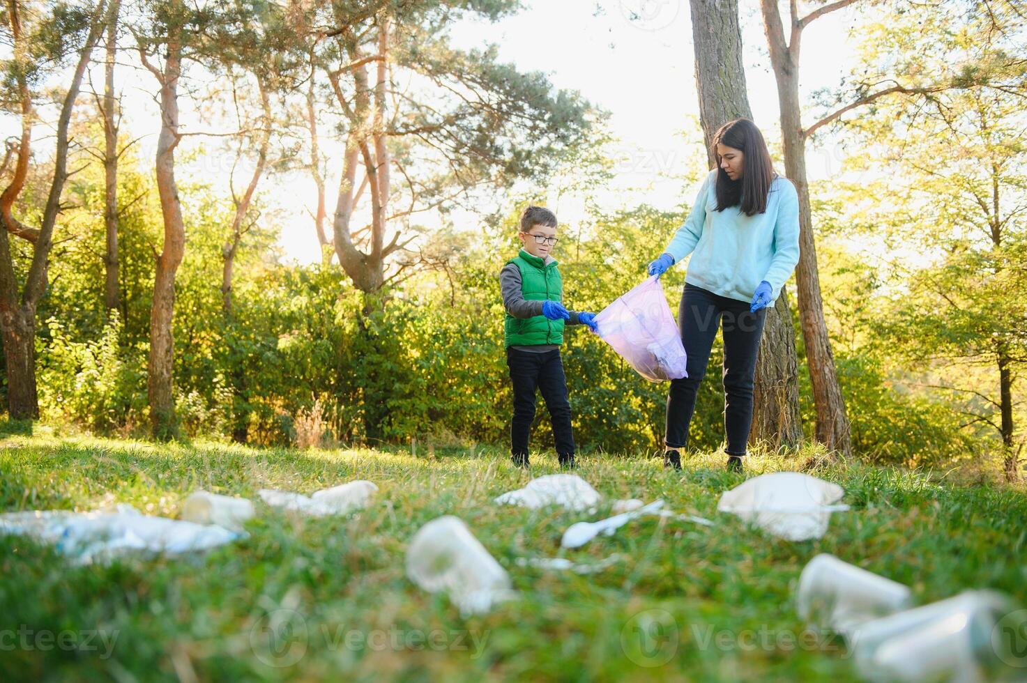 Woman volunteer and little boy picking up the plastic garbage and putting it in biodegradable trash-bag outdoors. Ecology, recycling and protection of nature concept. Environmental protection. photo