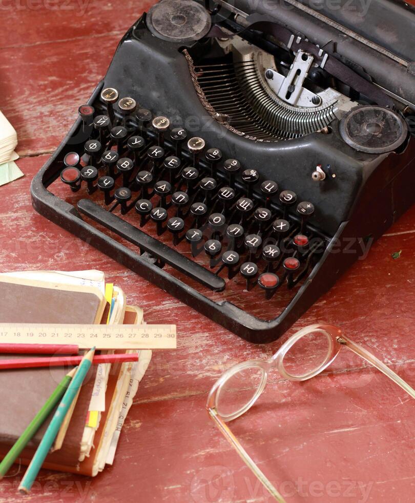 classic metal vintage typewriter on aged red painted wood with glasses and old notebooks photo