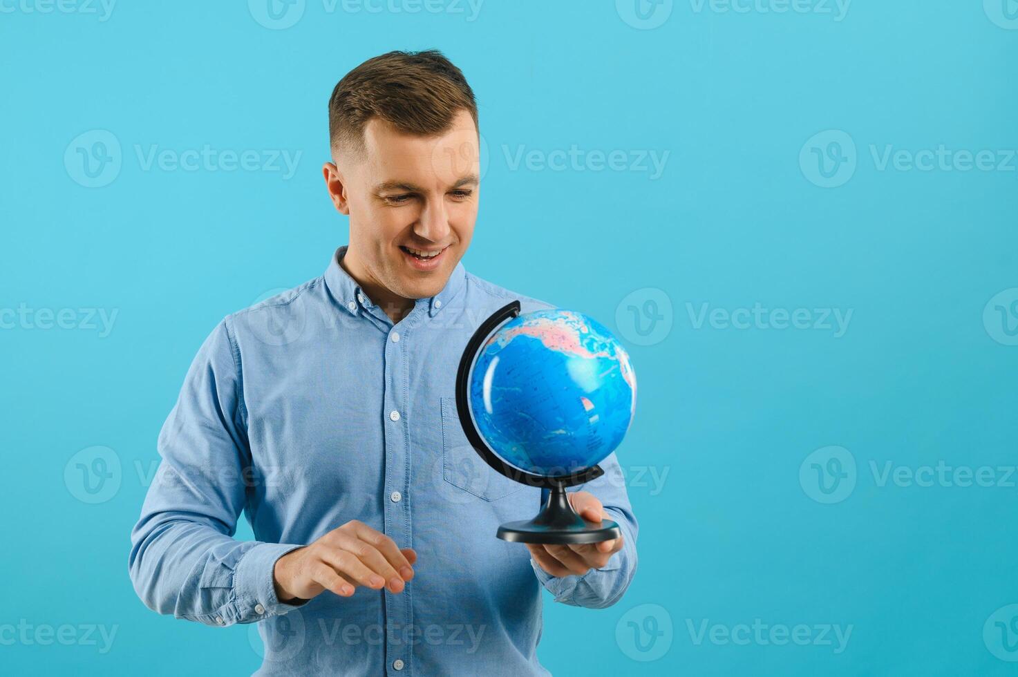 Excited traveler tourist man isolated on blue background. Passenger traveling abroad on weekends. Air flight journey concept. Holding world globe. photo