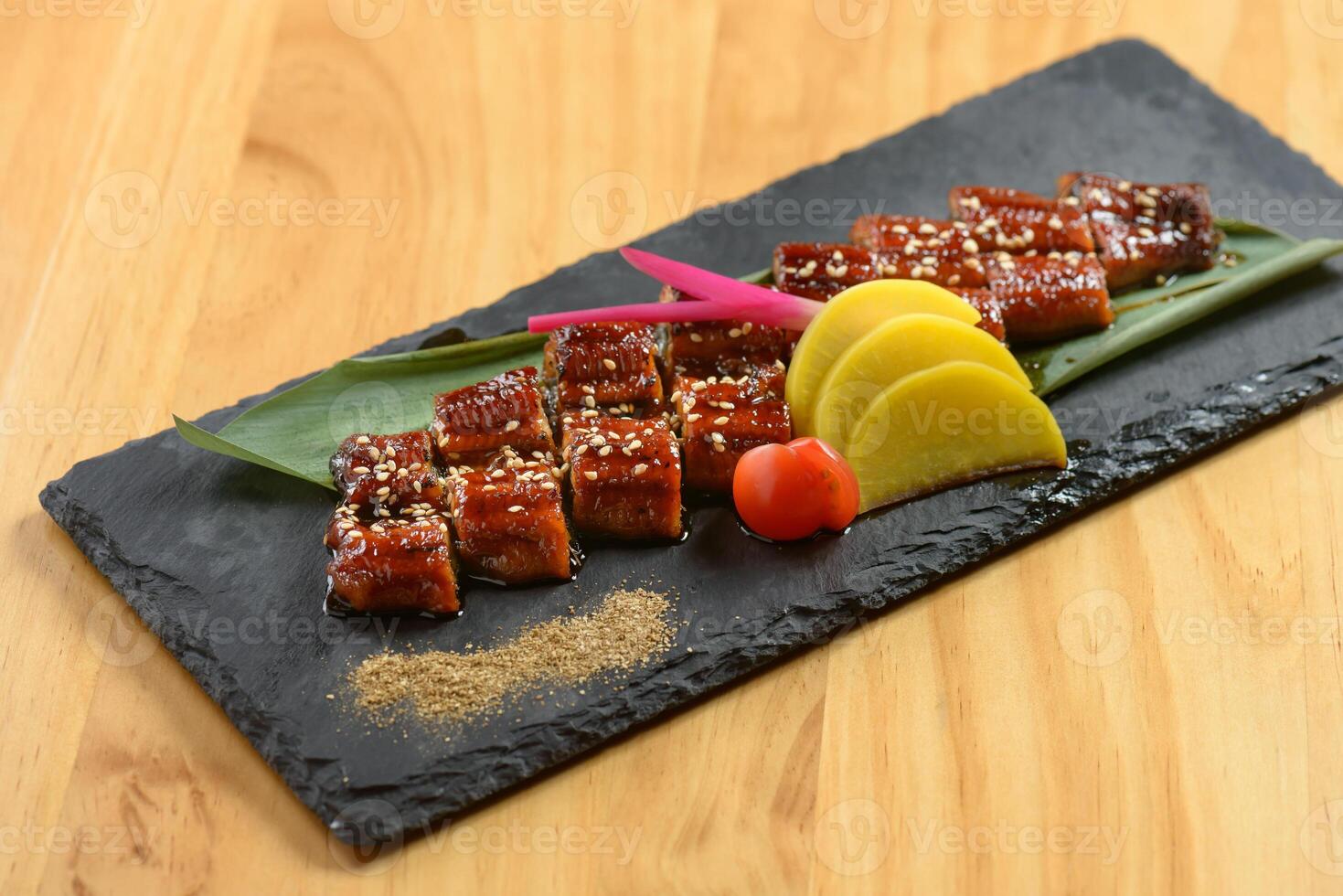 japanese cuisine Ultimate Unagi Kobayaki with lemon in black dish isolated on wooden background top view photo