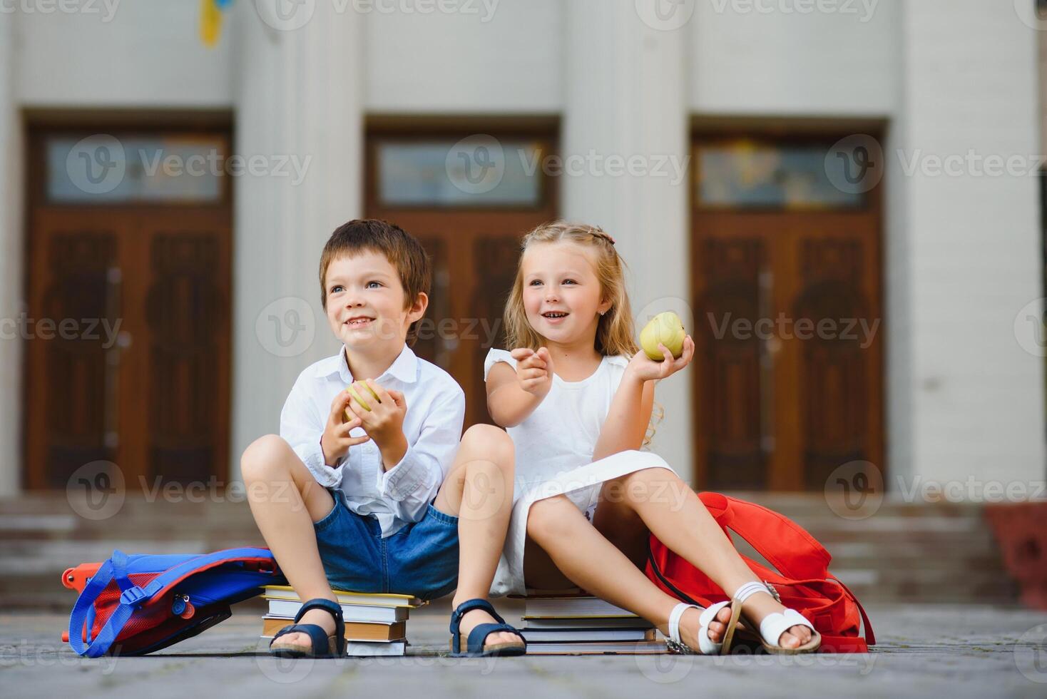 Two pupils of primary school. Boy and girl with school bags behind the back. Beginning of school lessons. Warm day of fall. Back to school. Little first graders. photo