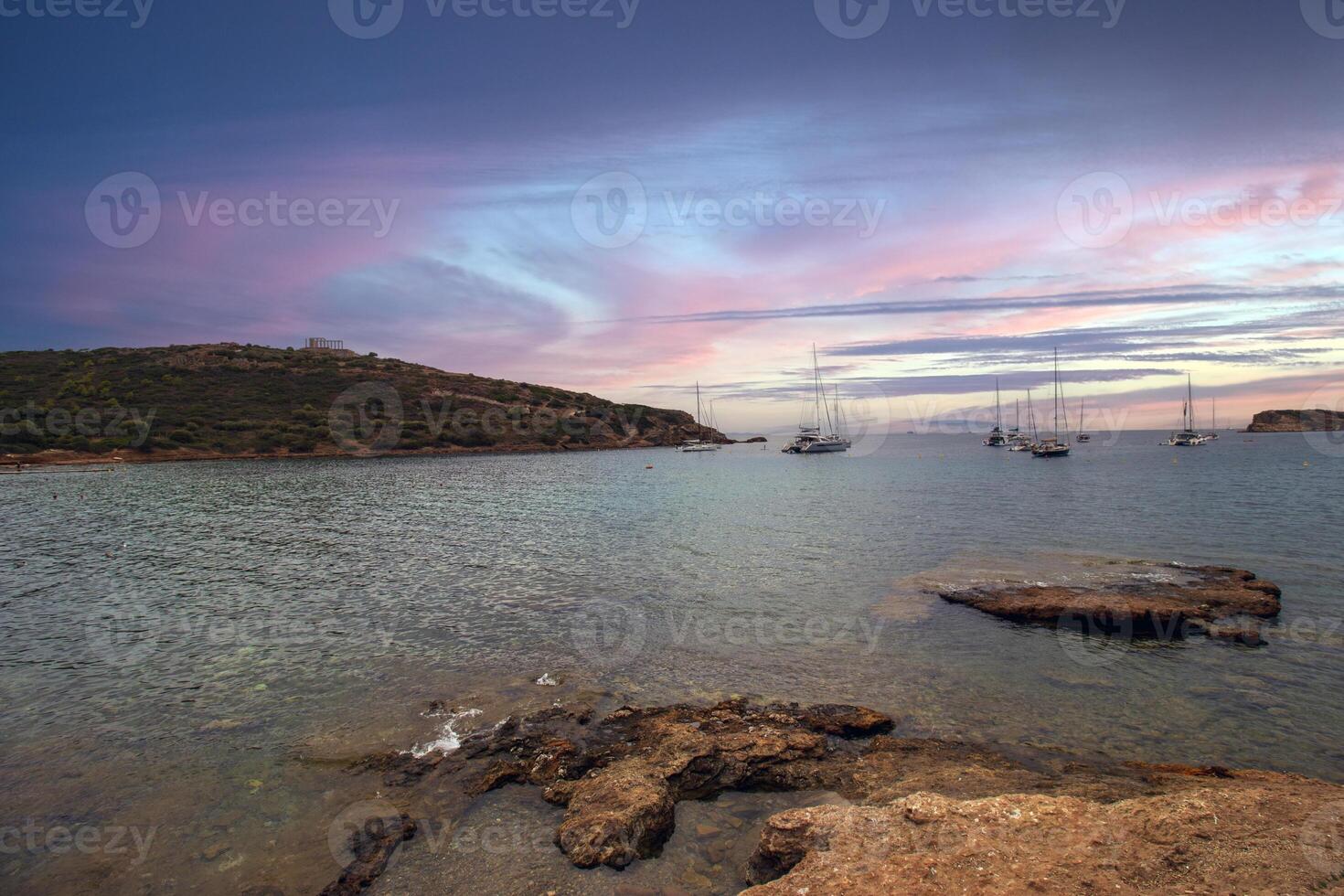 a el Egeo mar cerca el templo de Poseidón en sonión, Grecia, testigo un cautivador puesta de sol con vistoso nubes con barcos rodeando el majestuoso Poseidón templo foto