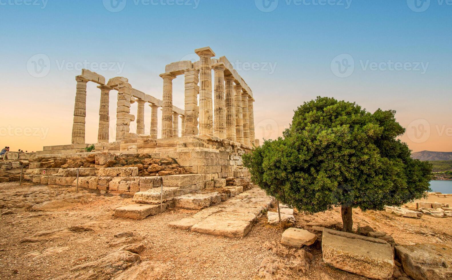 The famous temple of Poseidon in Greece with a green tree at sunset. In Greek mythology, the god of the sea. Cape Sounion, Ruins of the ancient temple with blue sky. photo