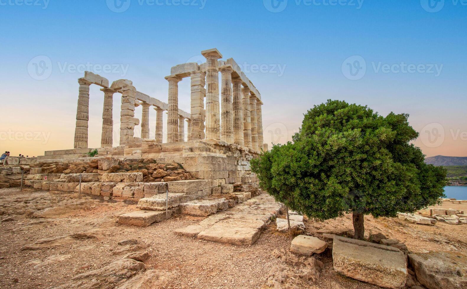 el famoso templo de Poseidón en Grecia con un verde árbol a puesta de sol. en griego mitología, el Dios de el mar. capa sonión, restos de el antiguo templo con azul cielo foto