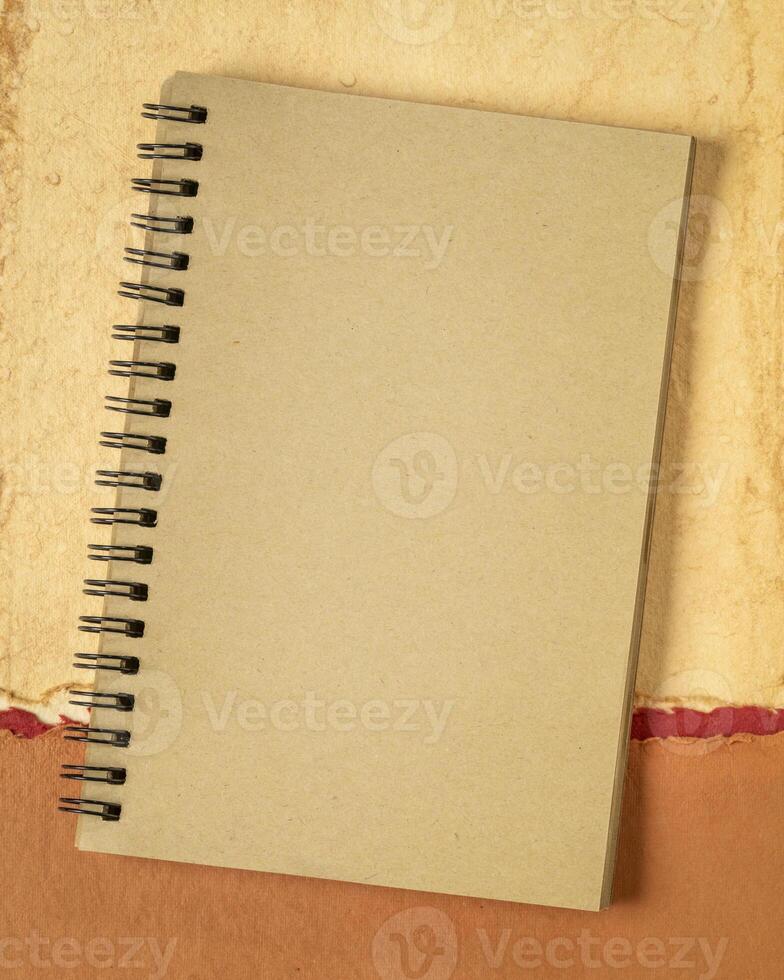 blank spiral notebook against abstract paper landscape, vertical poster photo