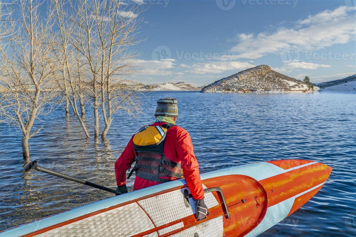 male paddler wearing a drysuit, life jacket and safety leash is starting workout on a long racing stand up paddleboard photo