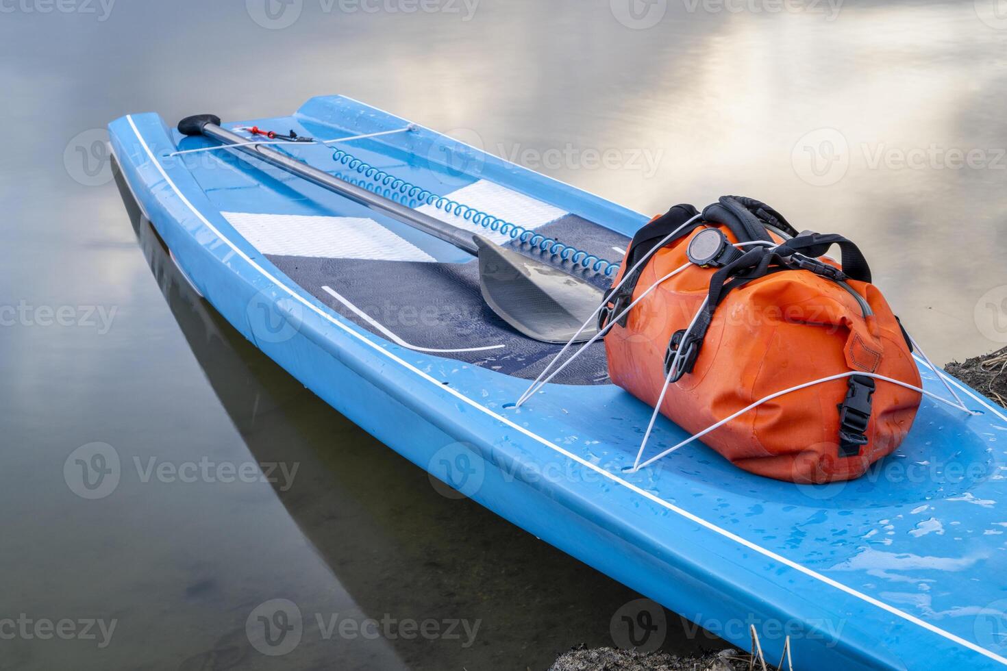 touring stand up paddleboard with a waterproof duffel, paddle and safety leash on a lake shore, early spring in Colorado photo