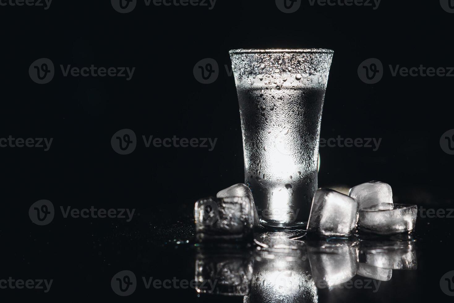 Vodka in shot glasses on black background, iced strong drink in misted glass. photo