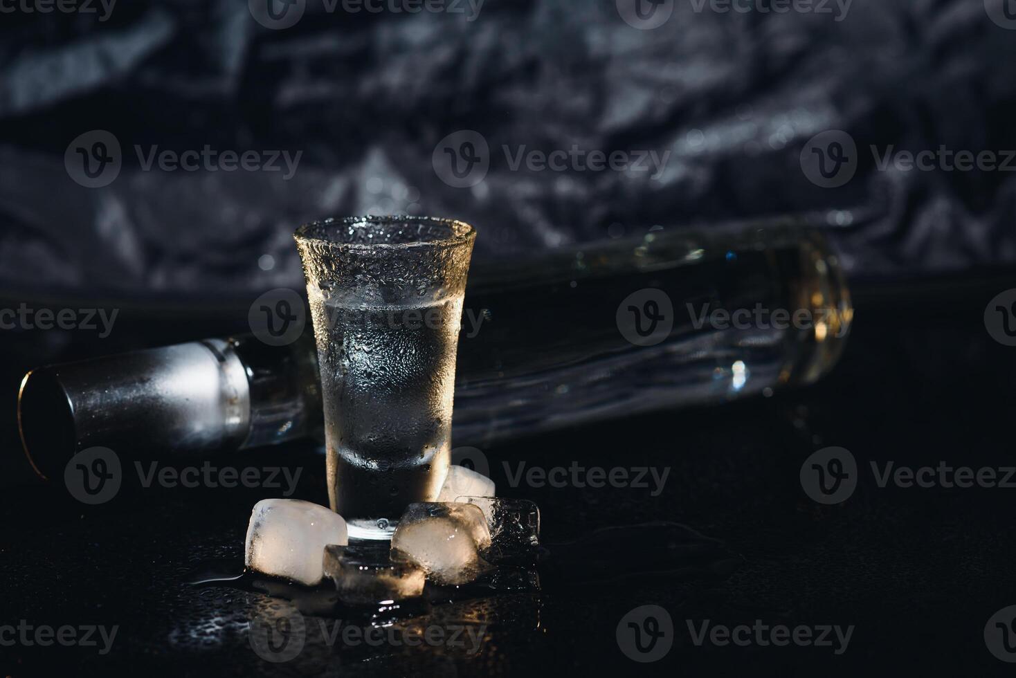 Vodka in shot glasses on black background, iced strong drink in misted glass. photo