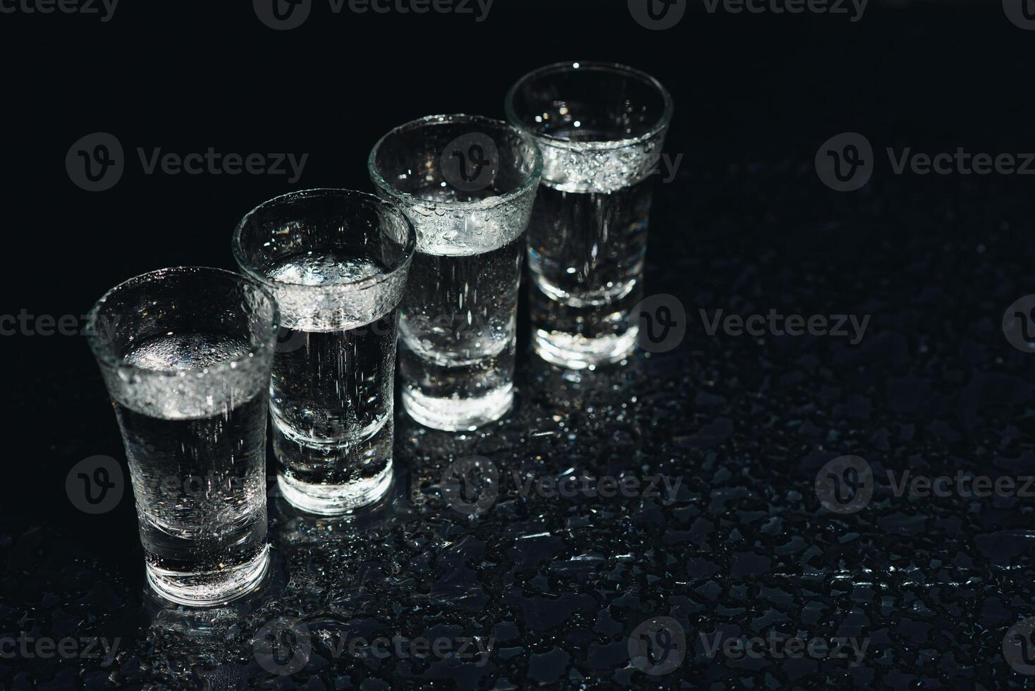 Vodka in shot glasses on black background, iced strong drink in misted glass. photo