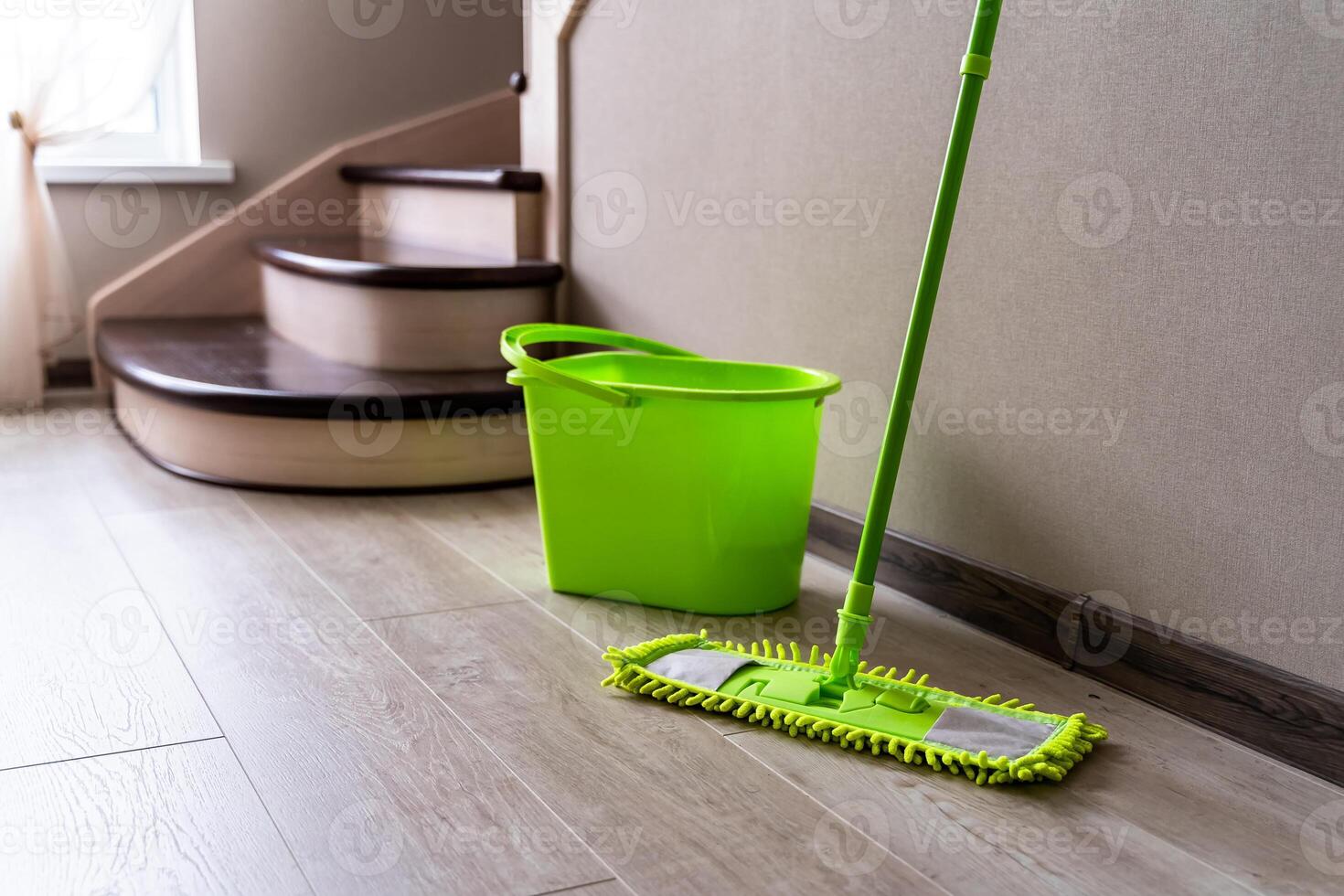 Green mop standing near white wall. Cleaning gear. Green plastic bucket. Householding. photo