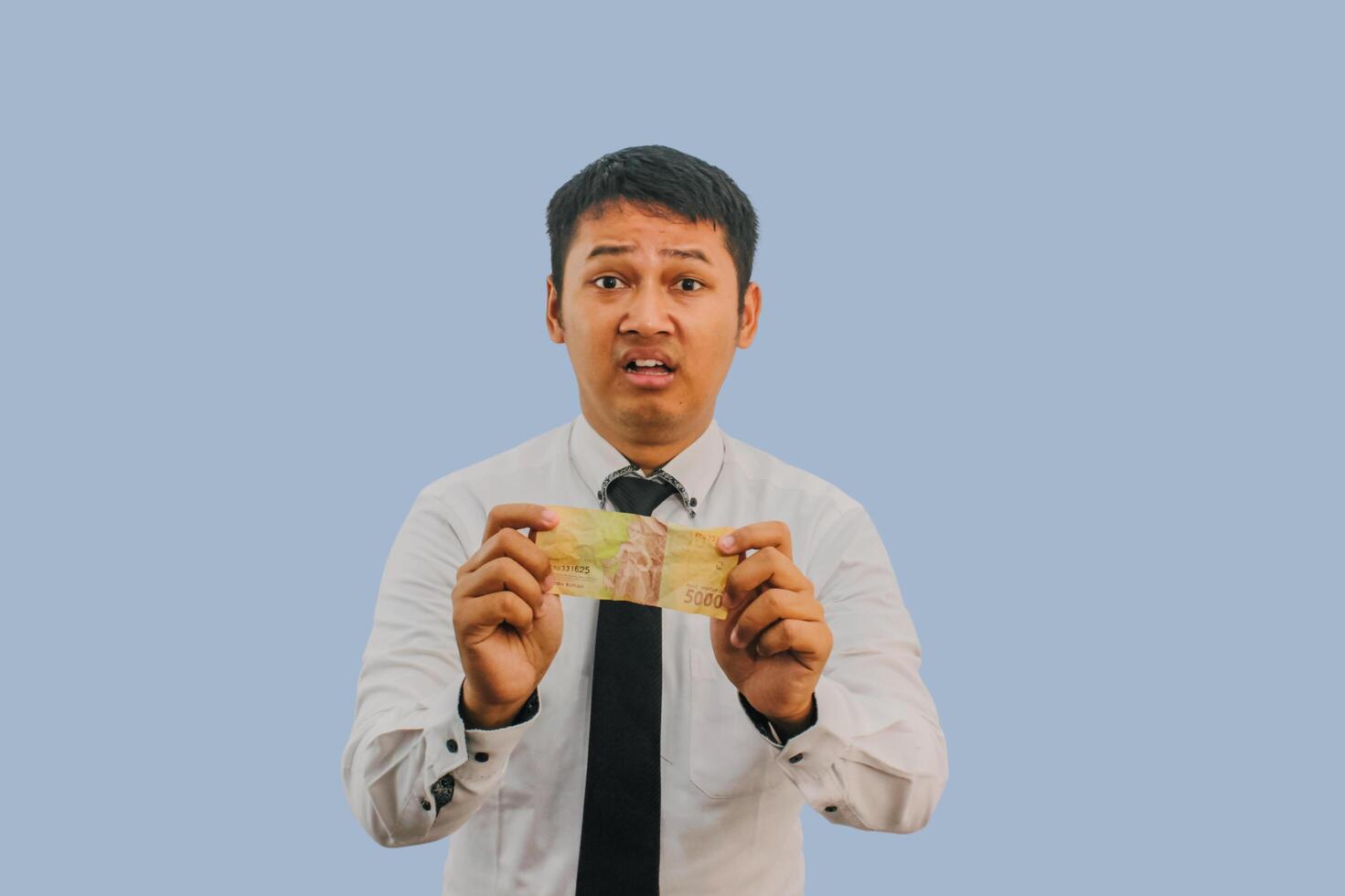 Adult Asian man showing sad expression while holding small amount of money photo