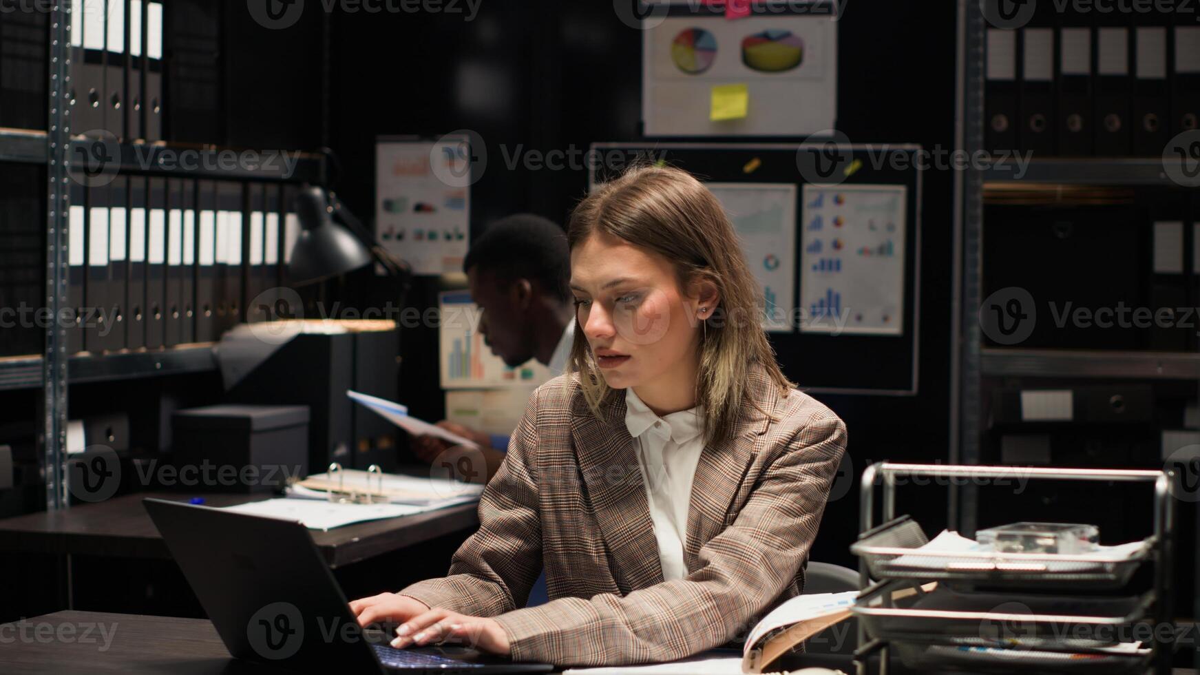 Detective inspector and male police officer investigate in office, examining files and evidence with expertise. Portrait shot of caucasian policewoman cross-checking information on paper with laptop. photo