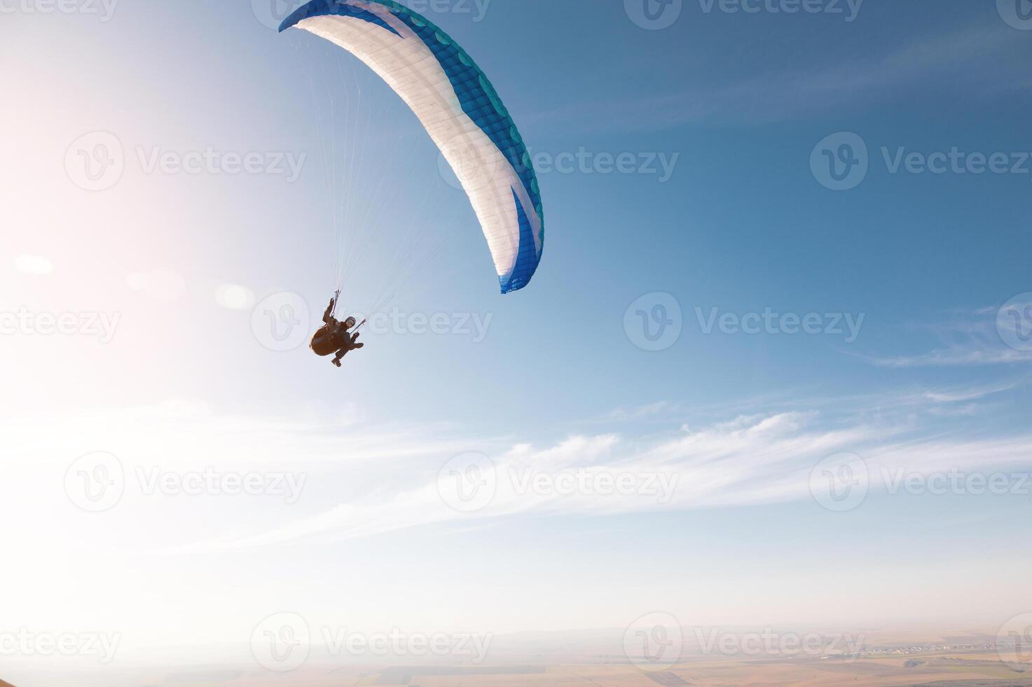 A paraglider with a blue parachute fly. A male flyght on the sky and lifts a paraglider into the air photo