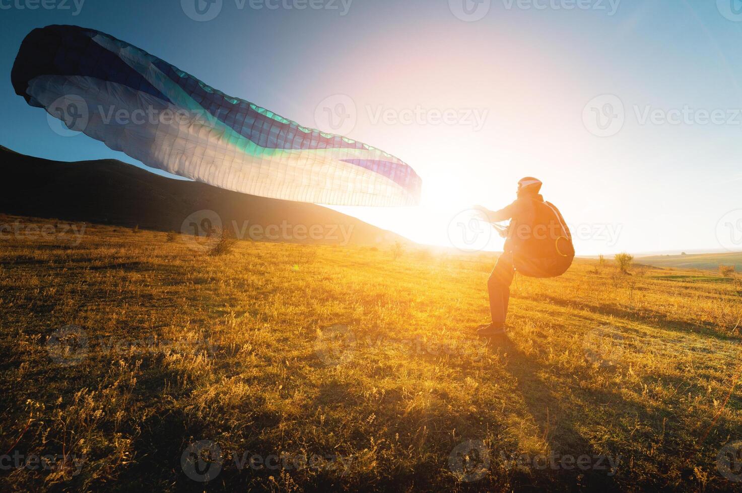 paraglider with a blue parachute takes off. A male athlete stands on the field and lifts a paraglider into the air photo