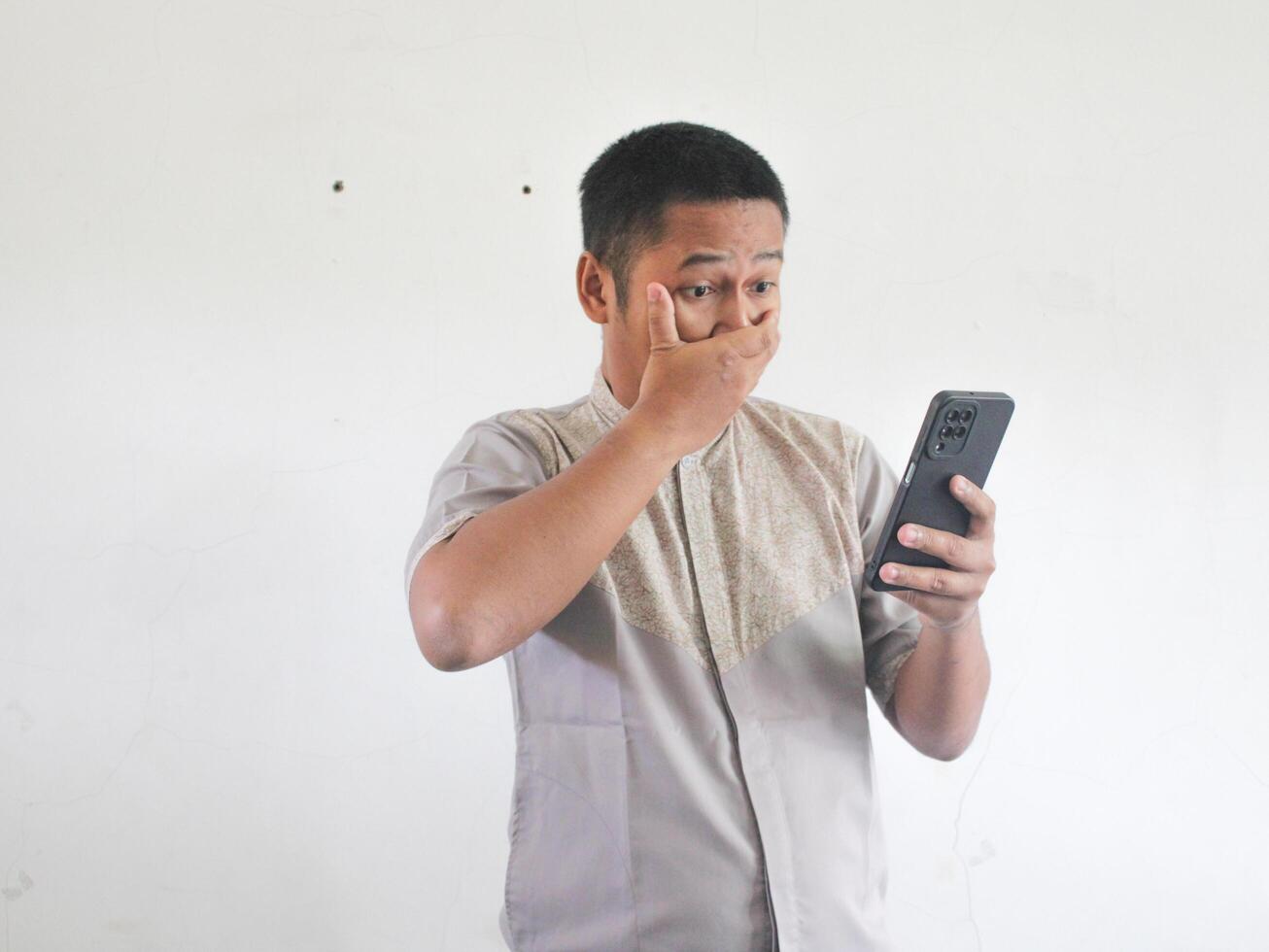 Adult Asian man showing shocked expression when looking to his phone photo