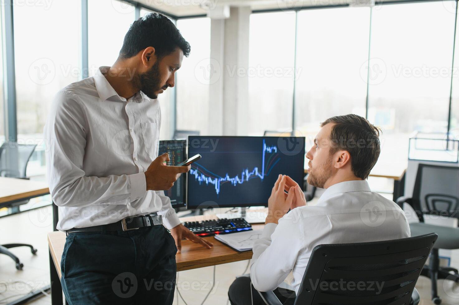 Two men traders sitting at desk at office together monitoring stocks data candle charts on screen analyzing price flow smiling cheerful having profit teamwork concept photo