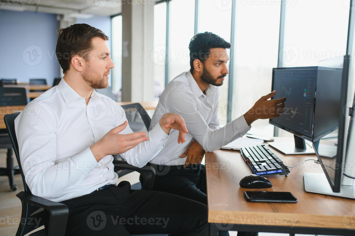 Two men traders sitting at desk at office together monitoring stocks data candle charts on screen analyzing price flow smiling cheerful having profit teamwork concept photo