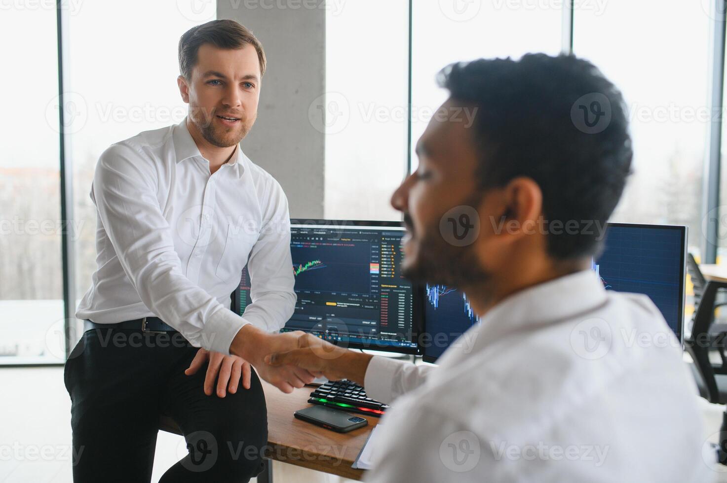 Two men traders sitting at desk at office together monitoring stocks data candle charts on screen analyzing price flow smiling cheerful having profit teamwork concept photo