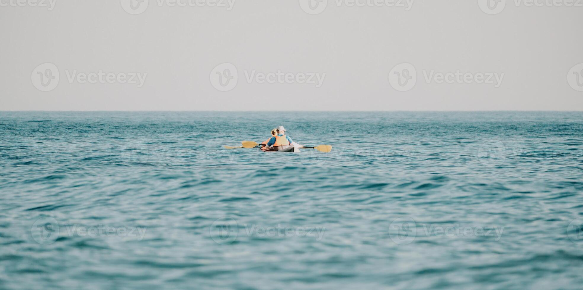 Happy couple kayaks in an inflatable kayak on the sea at sunset. Couple kanoeing in the sea near the island with mountains. People kayaking in life jackets sail. Back view photo