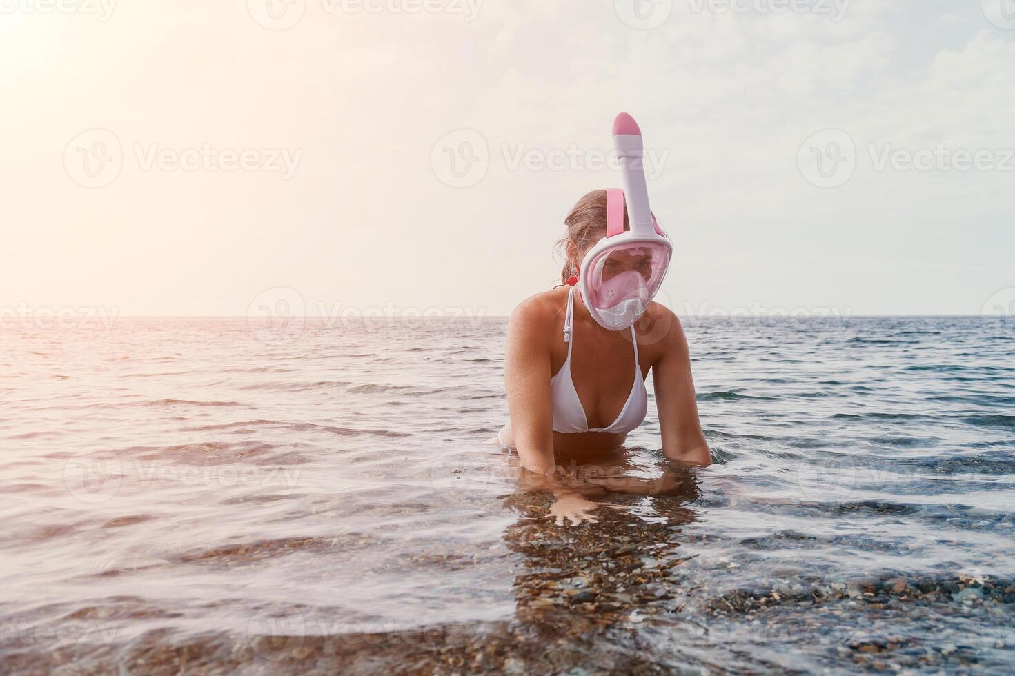 Young happy woman in white bikini and wearing pink mask gets ready for sea snorkeling. Positive smiling woman relaxing and enjoying water activities with family summer travel holidays vacation on sea. photo