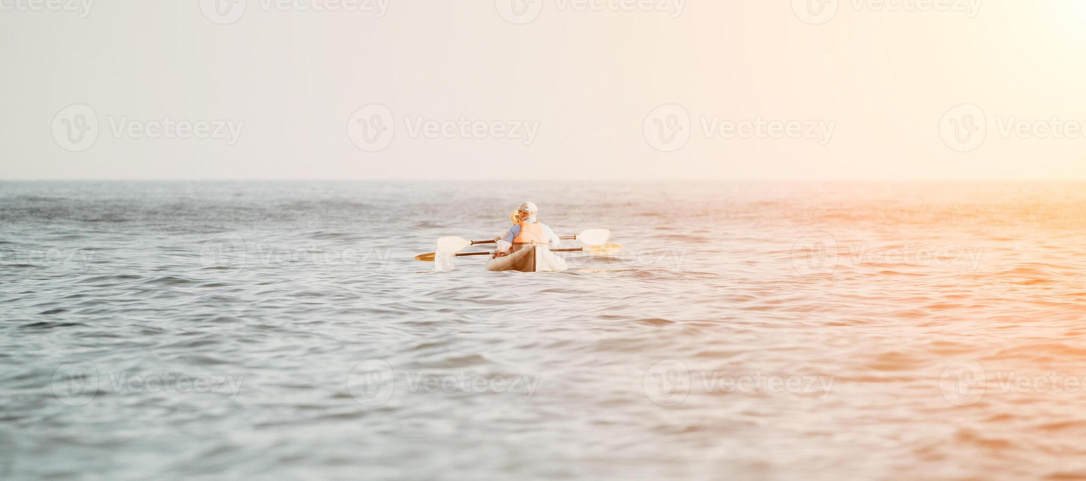 Happy couple kayaks in an inflatable kayak on the sea at sunset. Couple kanoeing in the sea near the island with mountains. People kayaking in life jackets sail. Back view photo