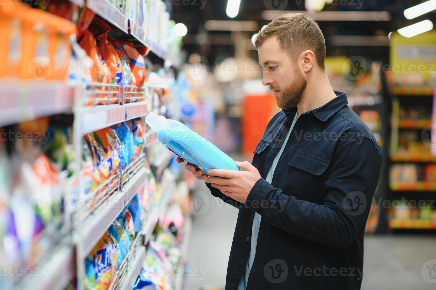 Young cheerful positive male customer making purchases in supermarket, buying household chemicals photo