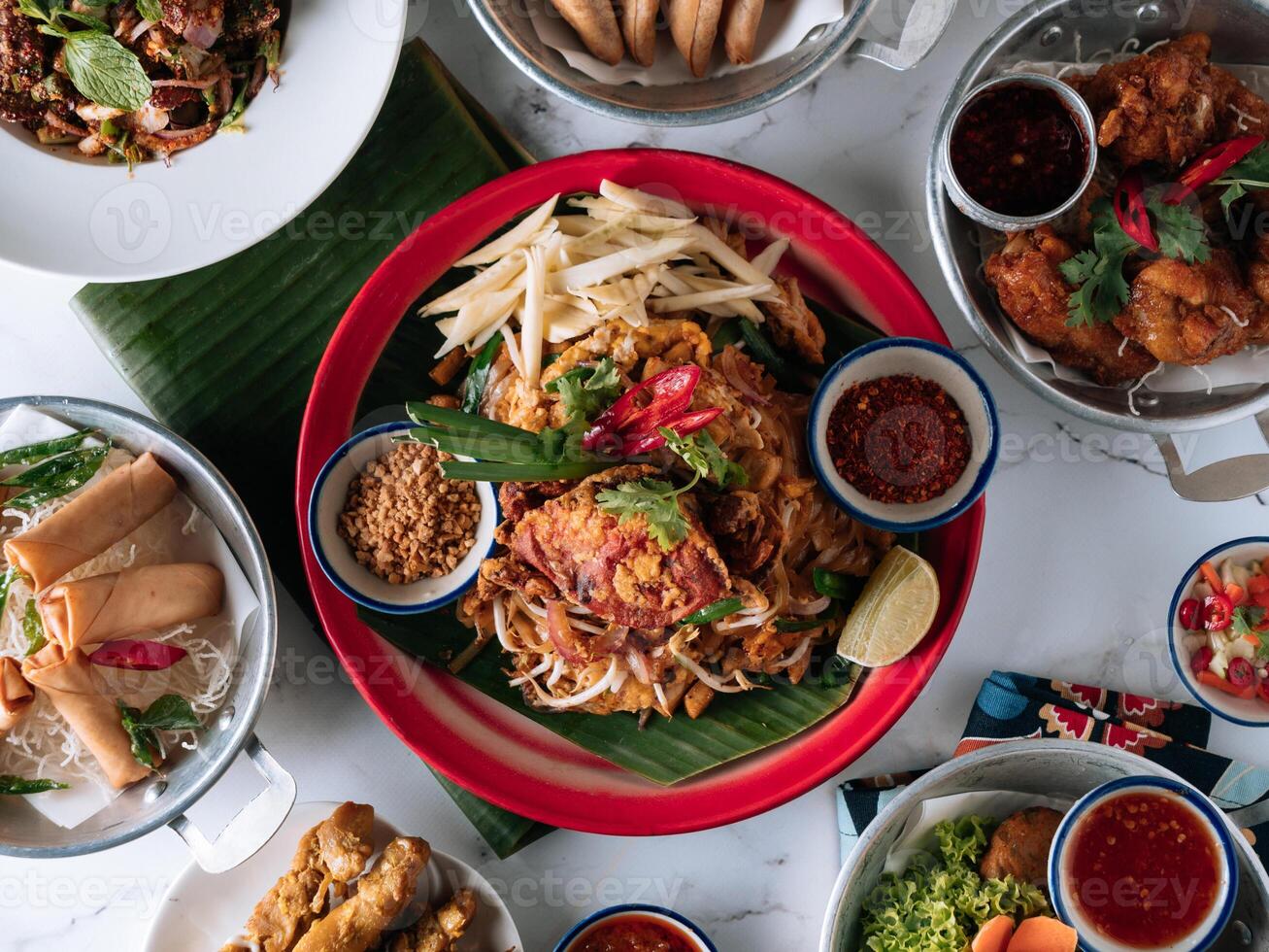 selectivo elección comida mesa cáscara cangrejo fideos , pollo satay, primavera rollo, curry samosa, pescado pastel, amigos tamboril, Cerdo tarro ensalada en un plato aislado en estera parte superior ver en gris mármol antecedentes foto