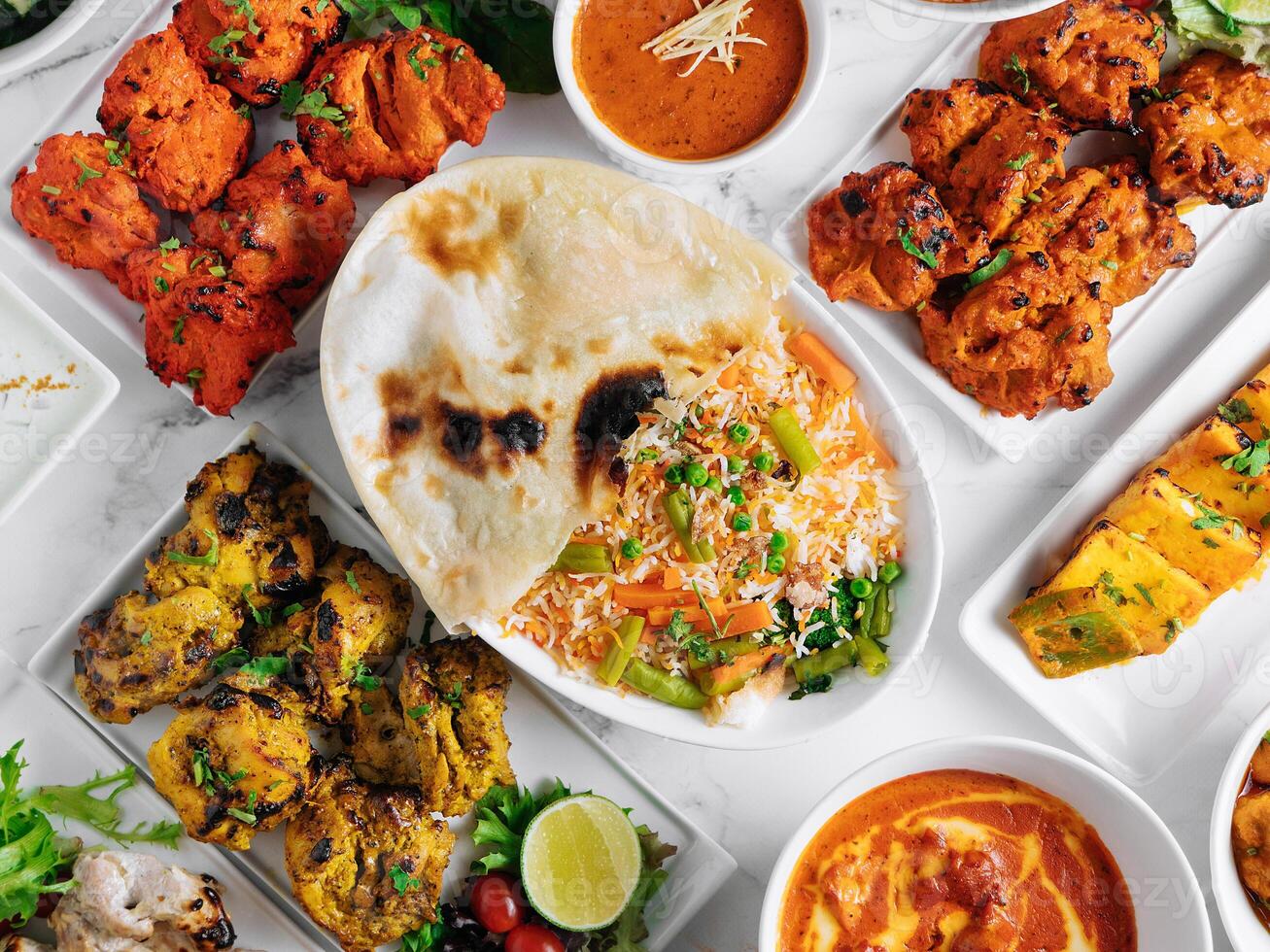 Assorted famous indian and pakistani food table vegetable biryani, Butter Chicken, paneer Chicken Tikka boti kebab, lime, Kali Mirchi, tomato sauce, raita, roti, salad, top view on grey background photo