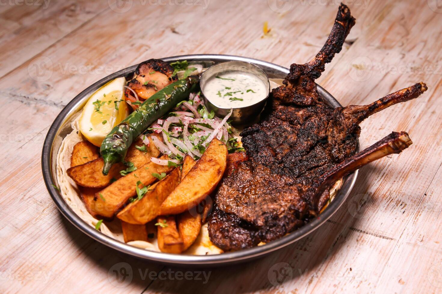 Riyash lamb chop with salad, wedges, lemon and dip served in dish isolated on background top view of arabic food photo