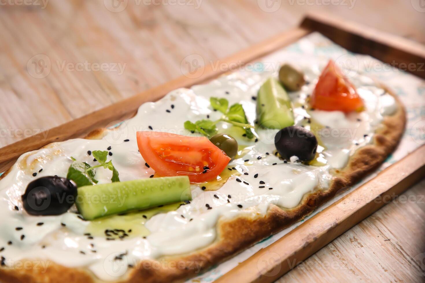 Labneh pizza bread with olives, tomato and cucumber served in wooden board isolated on background top view of Arabic Manaqeesh photo